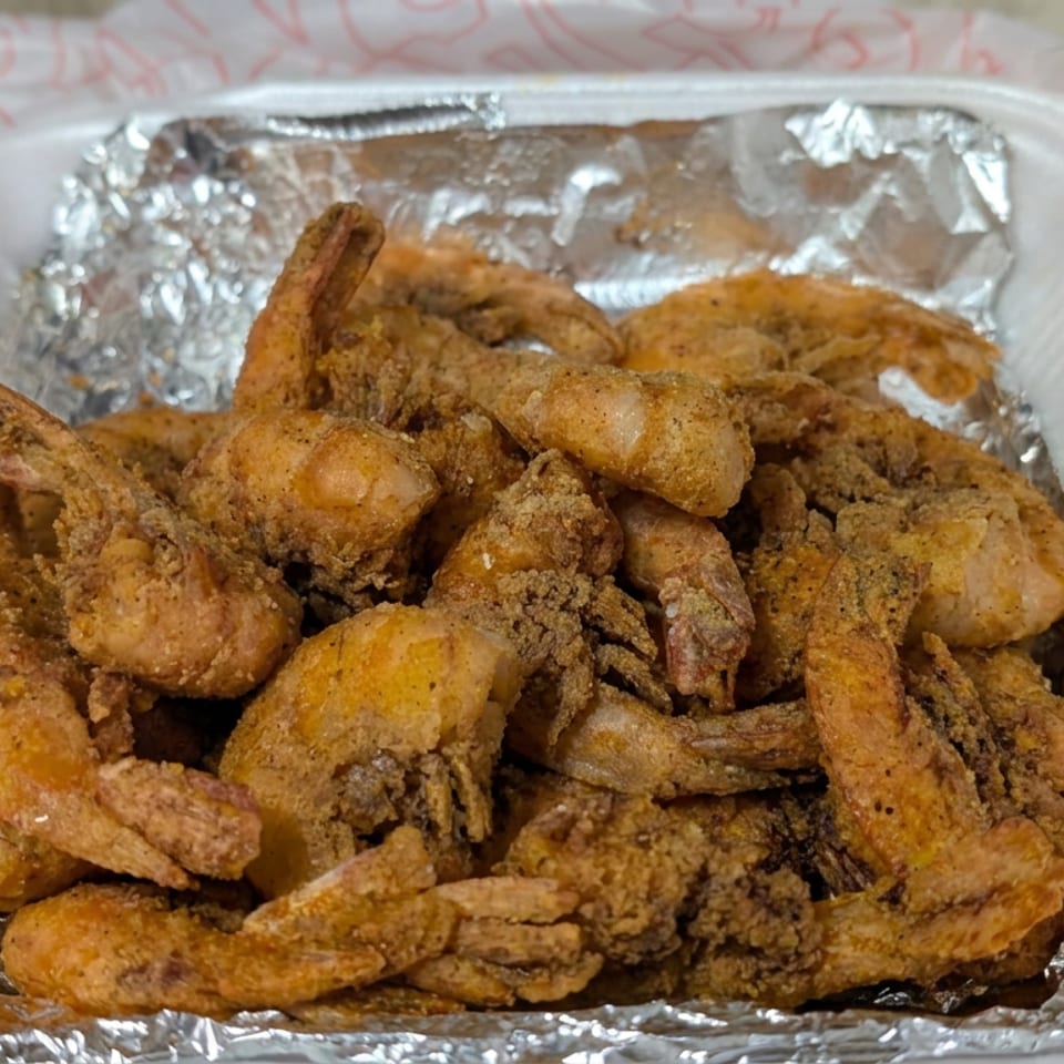 Foam container filled with golden-brown fried shrimp, lined with aluminum foil.