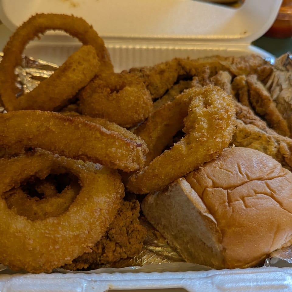 Takeout tray filled with fried chicken, onion rings, French fries, and a soft sandwich bun.