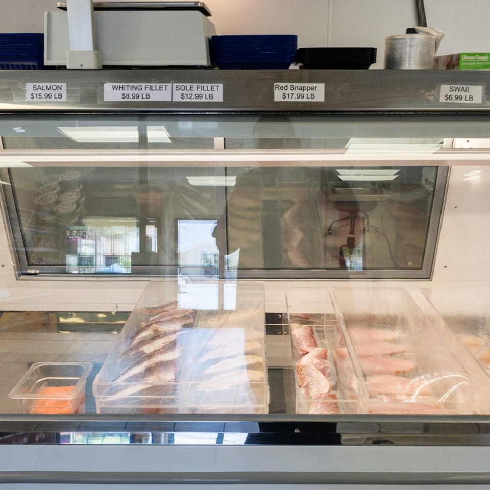 Refrigerated seafood counter displaying labeled smelt, salmon, whiting, sole, red snapper, swai, and catfish fillets.