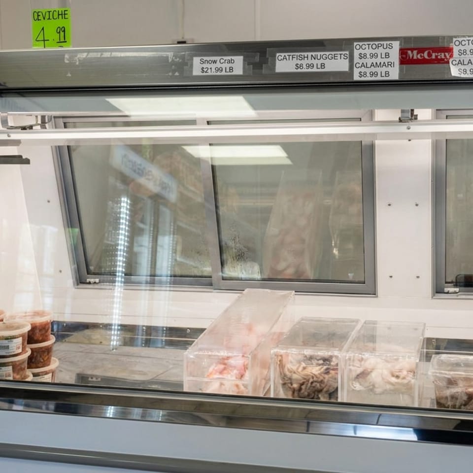 Refrigerated seafood display case with containers of seafood and signs listing ceviche, snow crab, catfish nuggets, octopus, and calamari.
